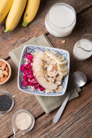 Hot and healthy food for Breakfast, Bowl of oatmeal porridge with bananas, apple, dragon fruit and almonds. Top viewの写真素材
