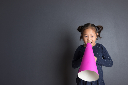 Asian thai age 6 year kid acting and shouting through pink paper megaphone. Communication concept.の写真素材