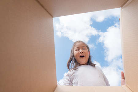 Asian kid girl age 6 year  unpacking and opening carton box, and looking inside with surpriseの写真素材