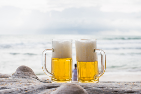 Glass mug of beer on a beach at sunsetの写真素材