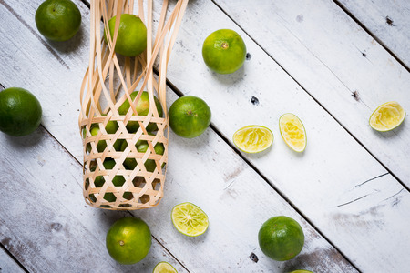 Lime in wicker round bamboo basket on white wooden backgroundの写真素材