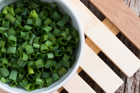 Chopped spring onions in white bowl on wooden tableの写真素材