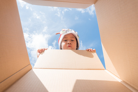 Asian kid girl age 6 year  unpacking and opening carton box, and looking inside with surpriseの写真素材