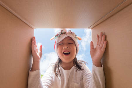 Asian kid girl age 6 year  unpacking and opening carton box, and looking inside with surpriseの写真素材