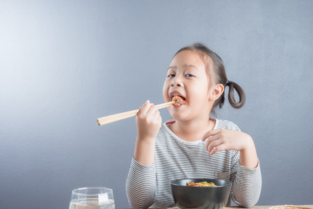 Happy Asian child age 6 years eating Stir fried yellow noodle "mee hokkian phuket", small thai girl eating noodles with chopsticks in  bowl with chopsticksの写真素材