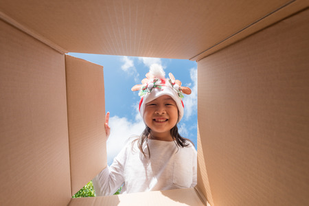 Asian kid girl age 6 year  unpacking and opening carton box, and looking inside with surpriseの写真素材