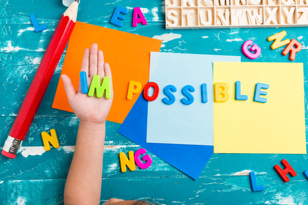 Children play plastic letters to combinations word IMPOSSIBLE on wood table.