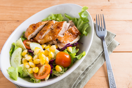 Grilled chicken fillet with colorful salad in white bowl on wooden backgroundの写真素材