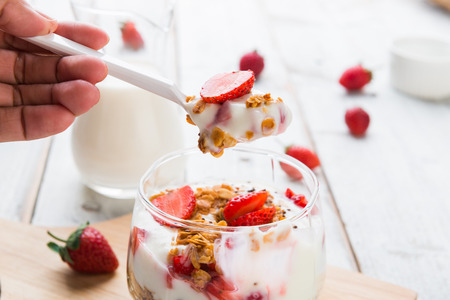 Strawberry , granola and yogurt healthy breakfast parfait on wooden background with hand and spoonの写真素材