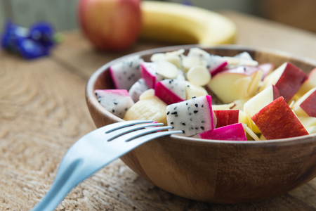Clean food healthy food concept , mixed fruit with apple, dragon fruit, banana and almond in wooden bowl on wooden tableの写真素材