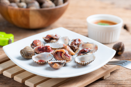 Steamed cockle ( Boiled cockles ) with spicy seafood sauce on wooden backgroundの写真素材