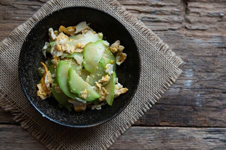Fresh chayote fruits (Sechium edulis) stir fried with egg and garlic in bowl on wooden backgroundの写真素材