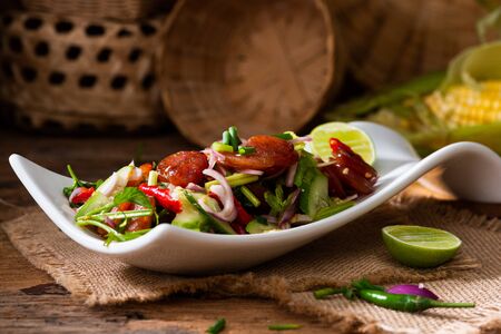 Spicy Chinese pork sausage with vegetable Thai salad in white plate on wooden backgroundの写真素材