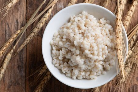 Cooked peeled barley grains in white bowl on wooden tableの写真素材