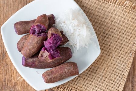 Steamed purple sweet potato in white plate eat with sugar and coconutの写真素材