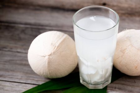 Fresh coconut juice in a glass with coconut white meat and peeled coconut on wood background.の写真素材