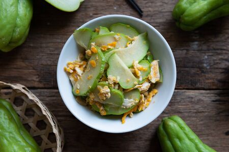 Fresh chayote fruits (Sechium edulis) stir fried with egg and garlic in bowl on wooden background