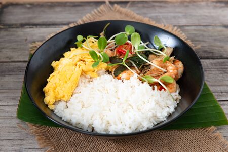Rice topped with stir-fried shrimp and basil, and fried eggs in white dish. Thai street food.の写真素材