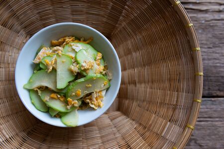 Fresh chayote fruits (Sechium edulis) stir fried with egg and garlic in bowl on wooden backgroundの写真素材