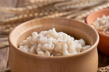 Cooked peeled barley grains in wooden bowl on wooden tableの写真素材