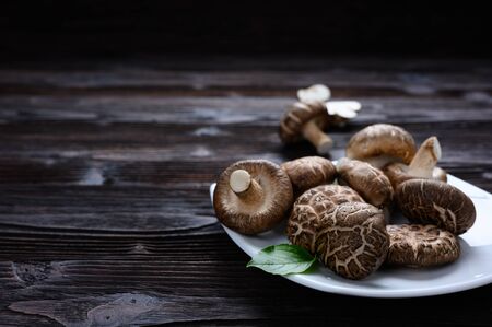 Shiitake mushrooms (Lentinus edodes) in white plate on the wooden background.