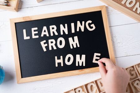  Learning From Home  words on a modern board on a white wooden surface, top view. Overhead, from...