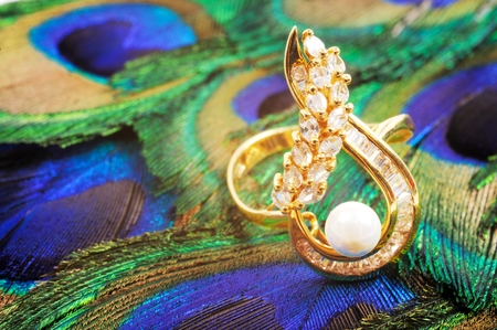 Golden ring with diamonds and pearl on the peacook featherの写真素材