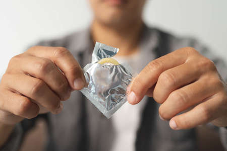 A man in a gray shirt is tearing a condom envelope to prevent contraception or sexually transmitted diseases.,World aids day.Safe sex concept.の写真素材