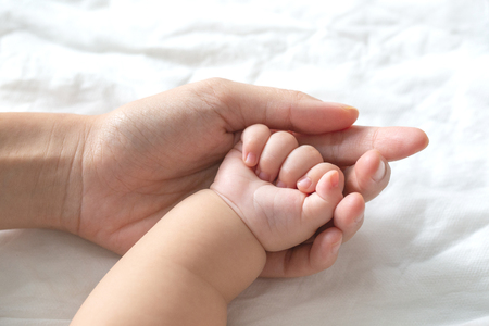 Mother uses her hand to hold her baby's tiny hand to make him feeling her love, warm, comfort and secure.の写真素材