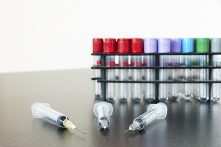 Three syringes and needles on the table with testtubes behindの写真素材