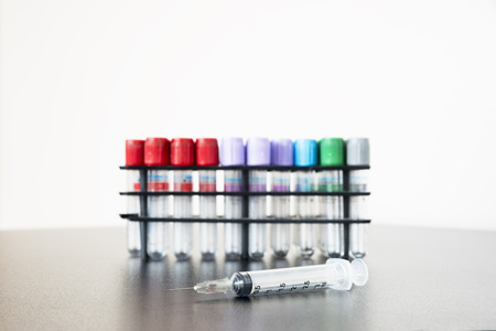 A syringe and needle on the table with testtubes behindの写真素材