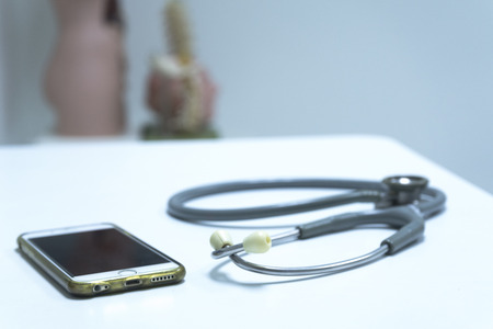 A grey stethoscope and smartphone on the doctor table with artificial human model in the backgroundの写真素材