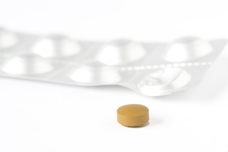Macrophotography of a yellow tablet of medication and blister package on the white backgroundの写真素材