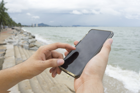 A man using left index finger for texting cellphone on the beachの写真素材