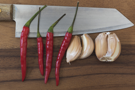 Knife, garlics and chillies on wooden chopping boardの写真素材
