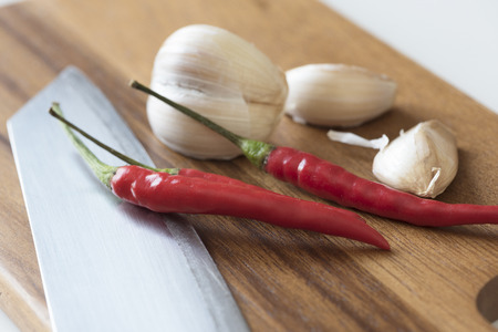 Close-up view of red chillies, garlics and knife on wooden chopping boardの写真素材
