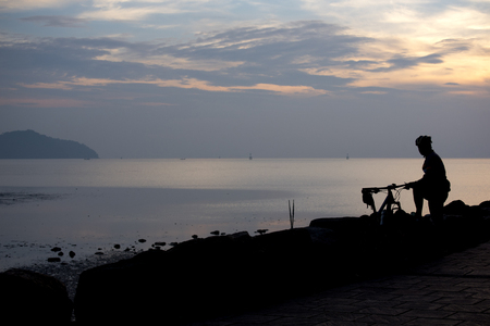 A silhouette cyclist relaxes near the shore during sunriseの写真素材