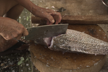 A man chopping a grouper fish on chopping block before cooking