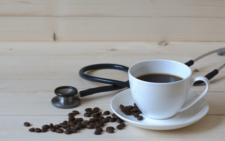 A cup of black coffee and coffe beans with a black stethoscope on the wooden backgroundの写真素材