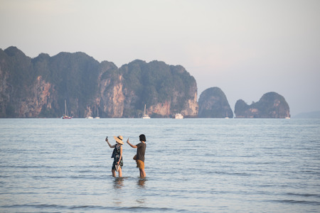 Krabi, Thailand-February 28, 2018: Two female asian tourists standing in the sea and using cellphone to take selfieのeditorial素材