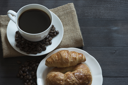 A cup of black coffee and beans, croissant and bread on wooden background for breafast mealの写真素材