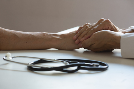 Doctor holding a patient hand for empathy and support in medical officeの写真素材