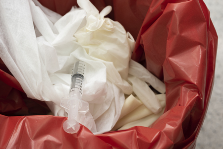 Used surgical gloves, gauzes and syringe in a red garbage bin for biohazard disposalの写真素材