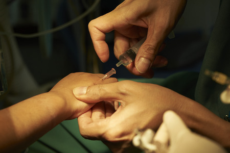 Anesthesiologist taking syringe out after accessing a patient venous line in operating room