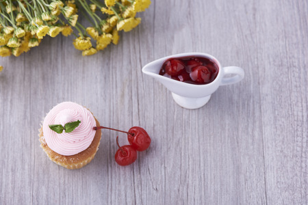 A delicious pink cupcake and cherries on wooden background
