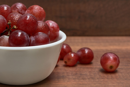 Delicious red grapes in a white bowl on wooden backgroundの写真素材