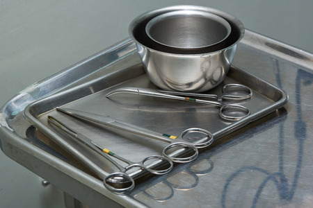 Used surgical instruments includings scissors, clamp, and cups on a stainless tray