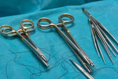 Needle holders with needles and sutures, surgical forceps and scissors on operating table