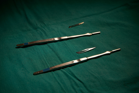 Two different sizes of surgical knife blades and holders on green table in operating roomの写真素材