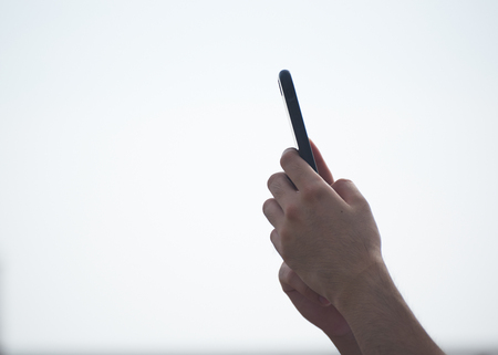 A man using both hands holding cellphone in the air on the beachの写真素材